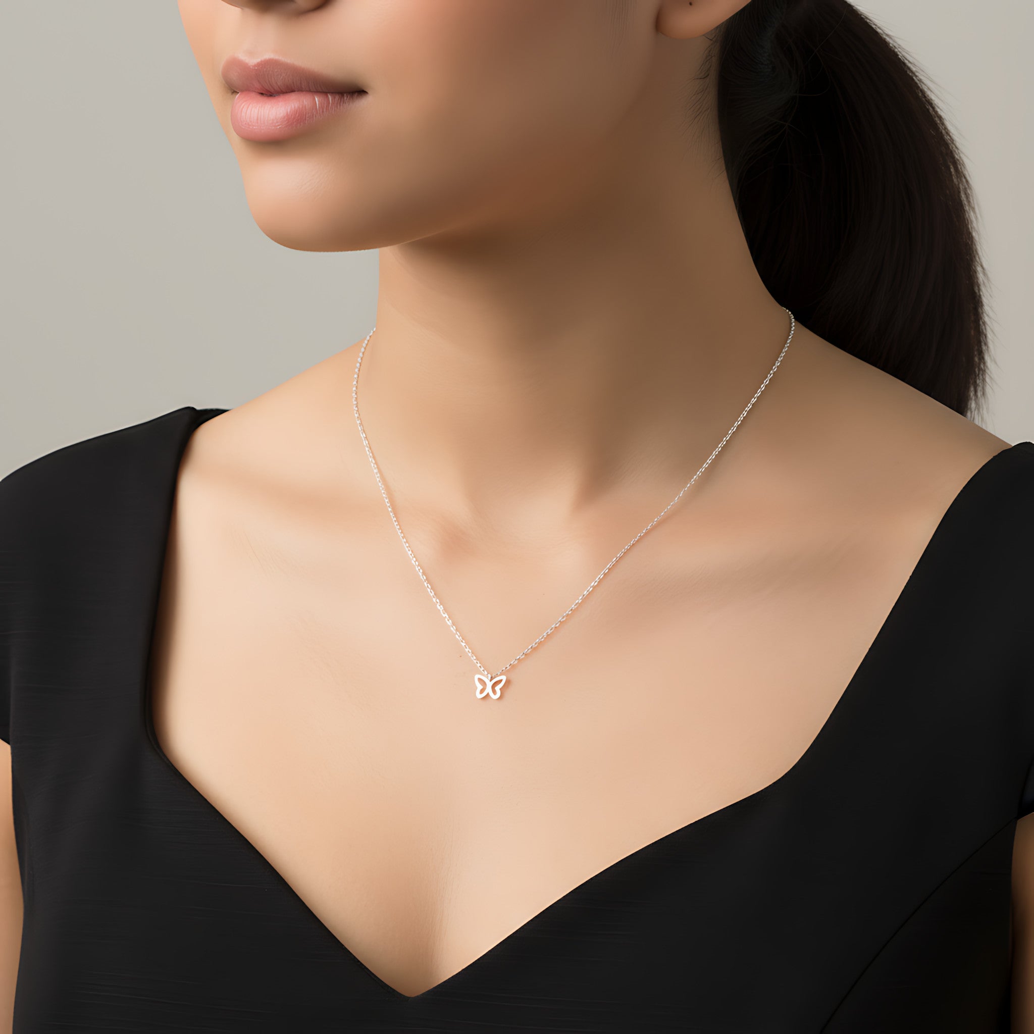Closeup of a female wearing a silver necklace with a small butterfly pendant against a neutral background