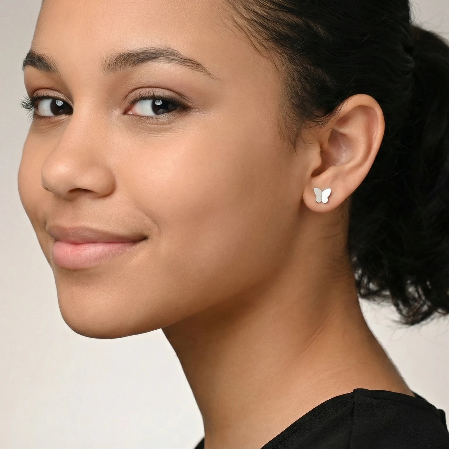 Close-up of a young girl wearing silver butterfly stud earrings against a neutral background