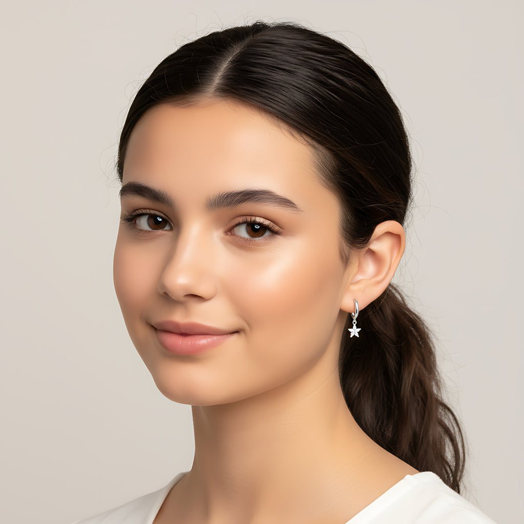 A girl with a ponytail wearing a silver star charm hoop earring against a plain background