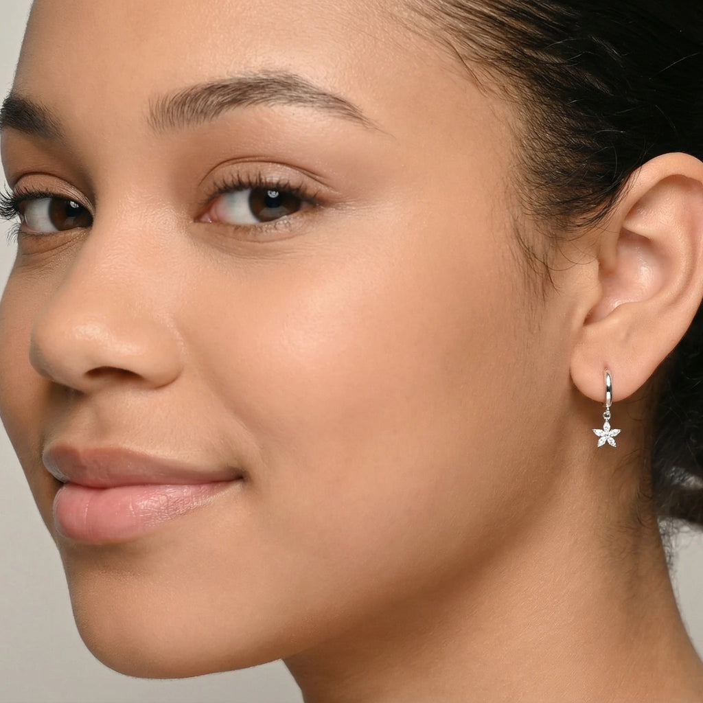 A closeup of a girl wearing a silver star charm hoop earring against a plain background