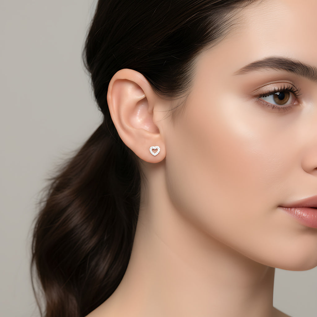 Close-up of a woman wearing a heart-shaped silver stud earring against a neutral background
