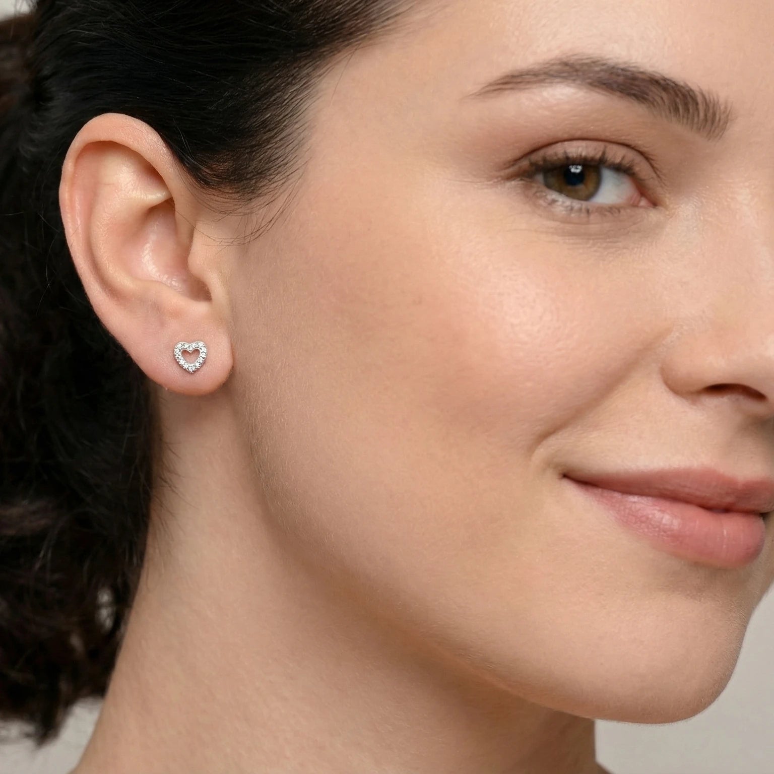Close-up of a woman wearing a heart-shaped silver stud earring against a neutral background