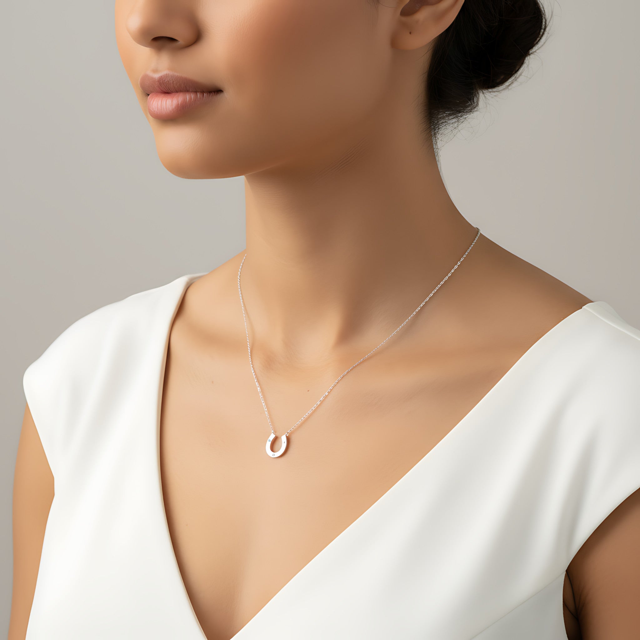 Woman wearing a delicate silver necklace with a small horseshoe pendant against a neutral background