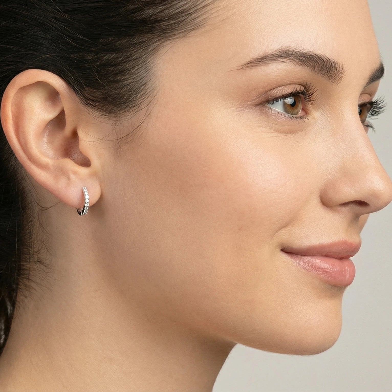 Close-up of an ear wearing a small CZ silver hoop earring with a blurred background