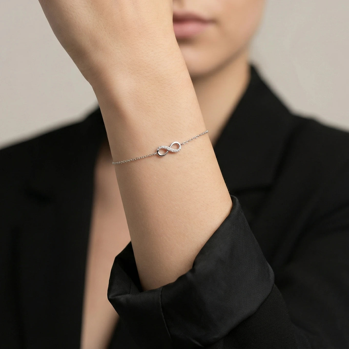 A female wearing a delicate silver cz infinity bracelet on a neutral background