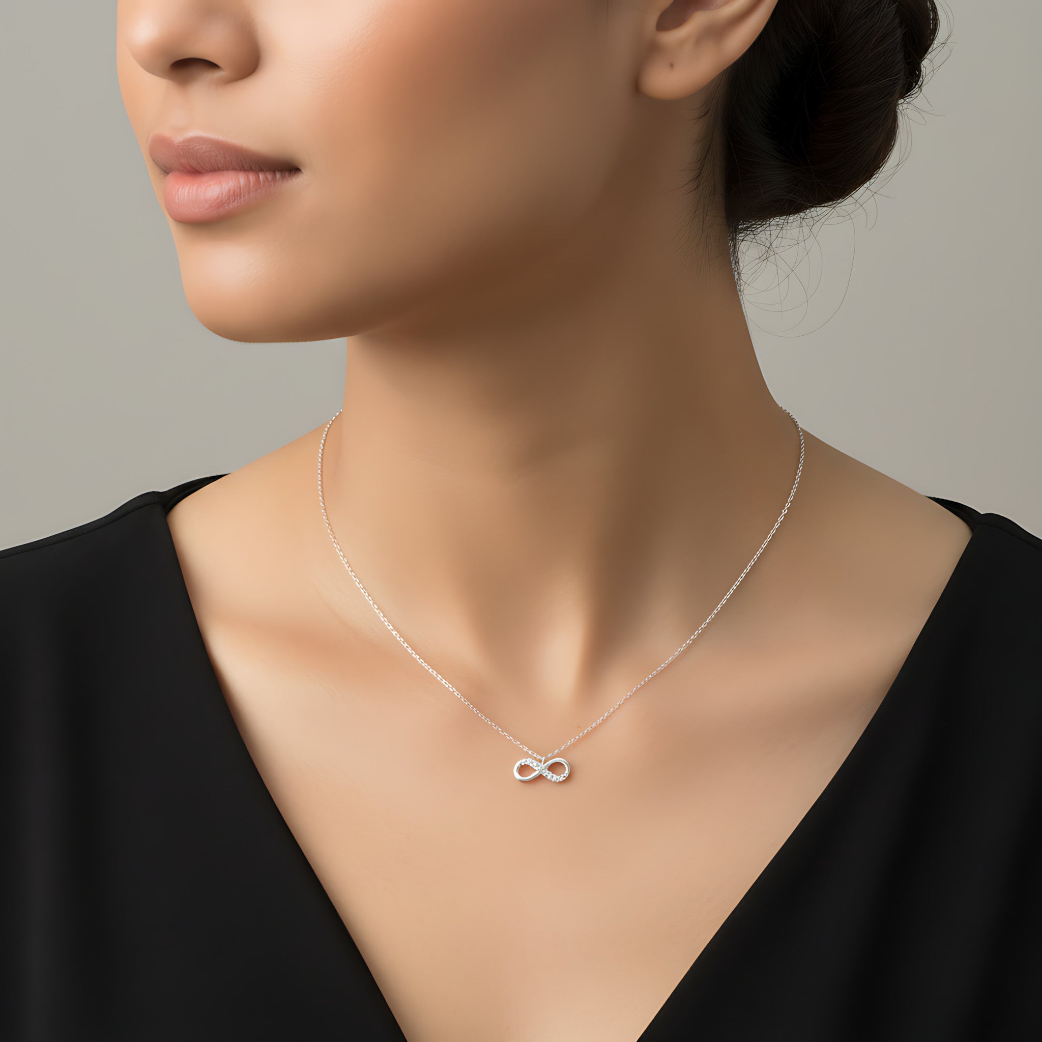 Woman wearing a silver necklace with an infinity symbol on a neutral background