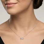 Woman wearing a silver necklace with an infinity symbol on a neutral background