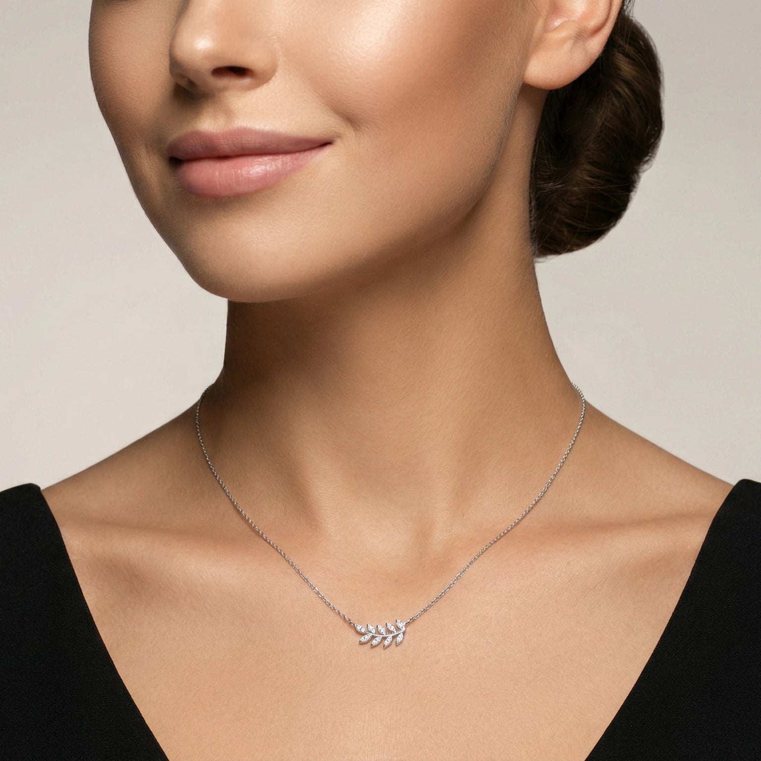 Closeup of a female wearing a silver necklace with a small olive leaf pendant against a neutral background