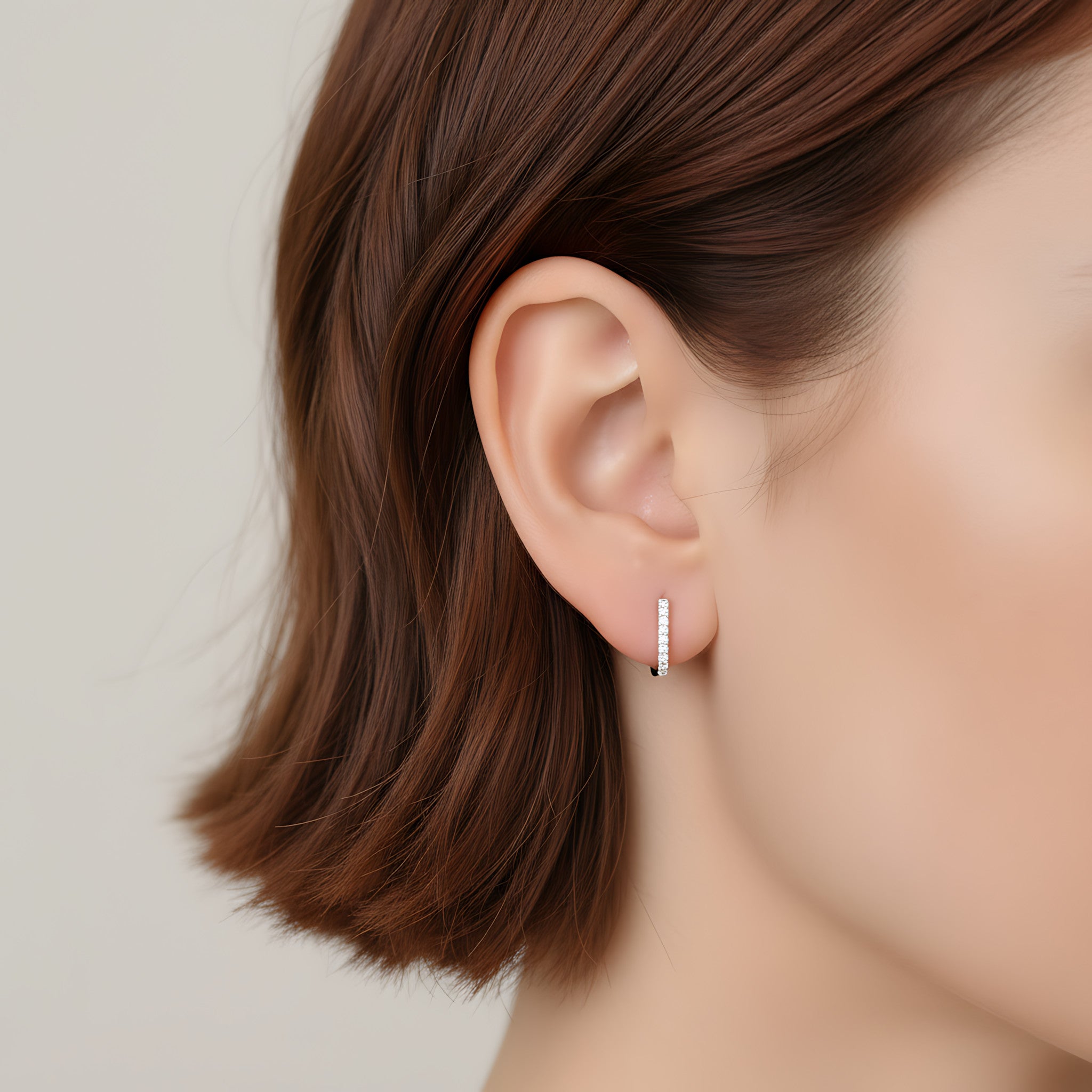 Close-up of an ear wearing a small CZ rectangle hoop earring with a neutral background