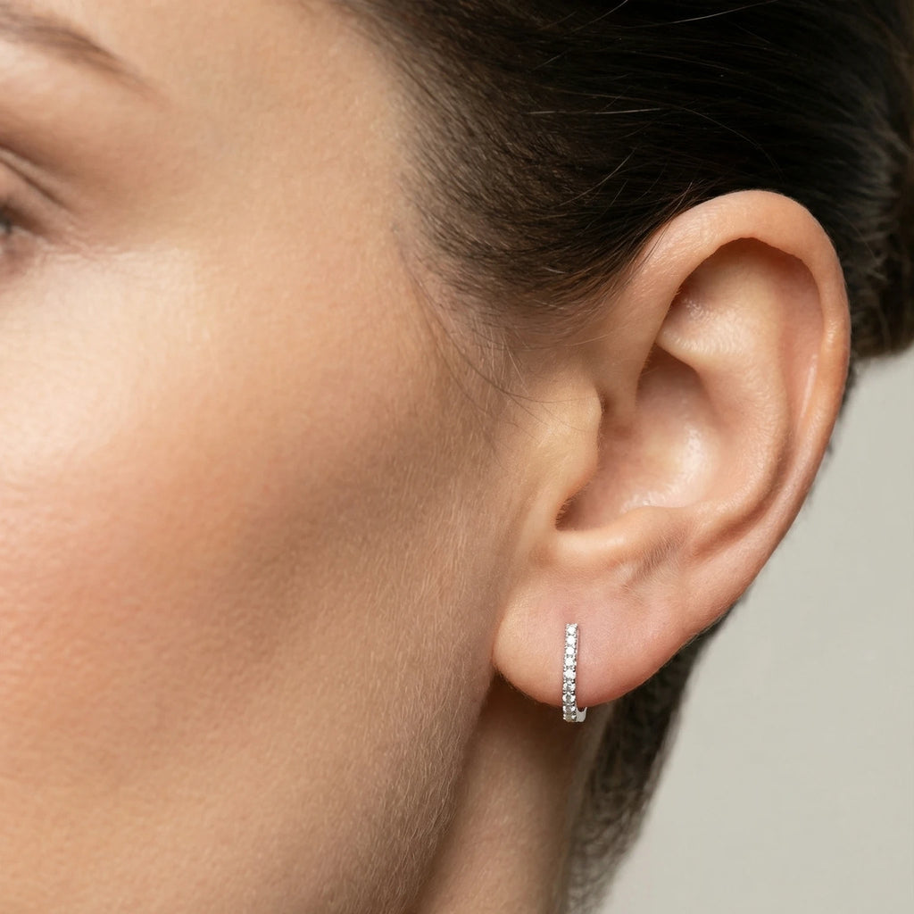 Close-up of an ear wearing a small CZ rectangle hoop earring with a neutral background