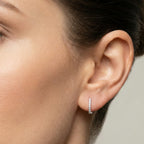 Close-up of an ear wearing a small CZ rectangle hoop earring with a neutral background