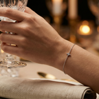 Hand holding a glass with a cz-star shaped silver bracelet on a blurred background