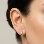 Close-up of an ear wearing a small CZ star silver hoop earring with a blurred background