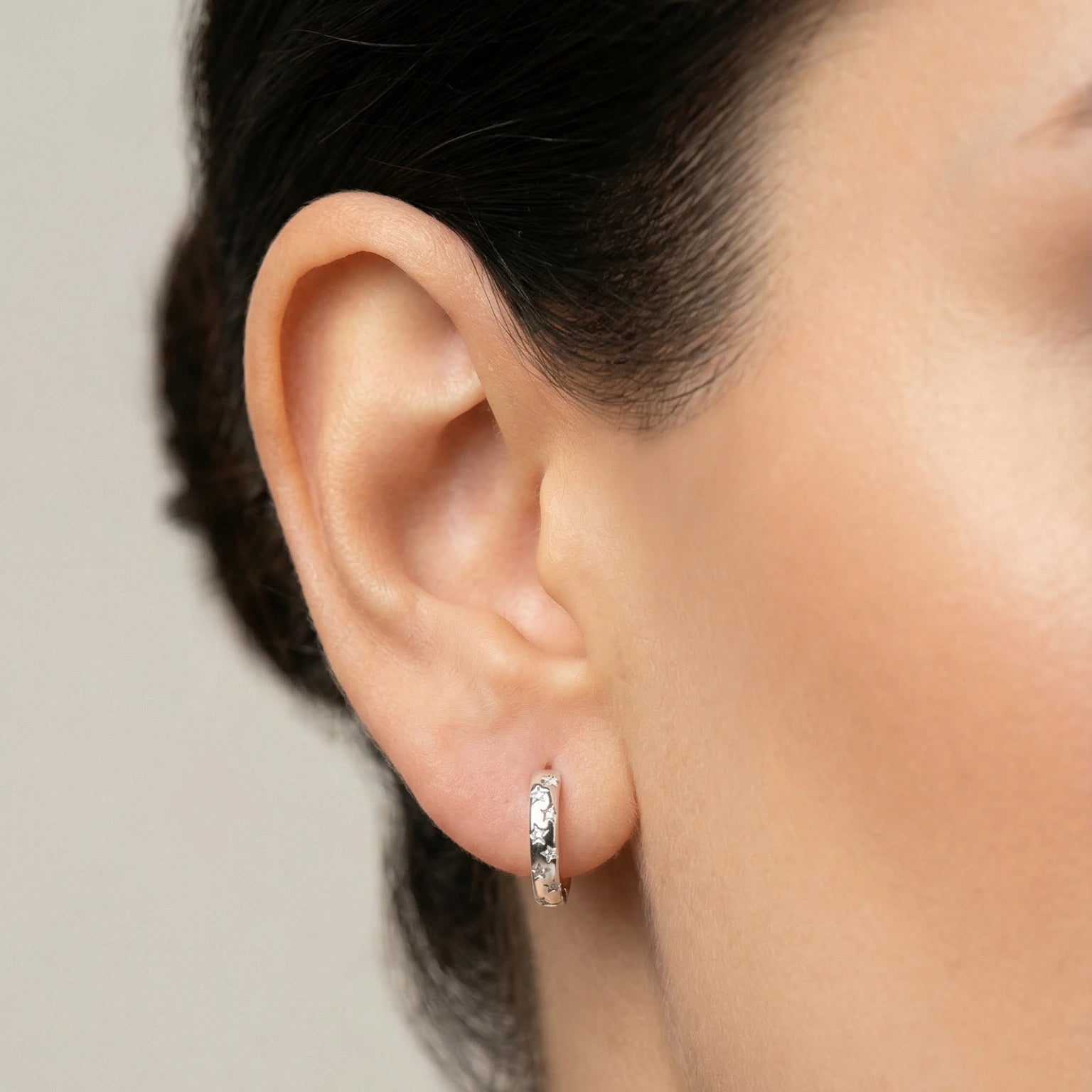 Close-up of an ear wearing a small CZ star silver hoop earring with a blurred background