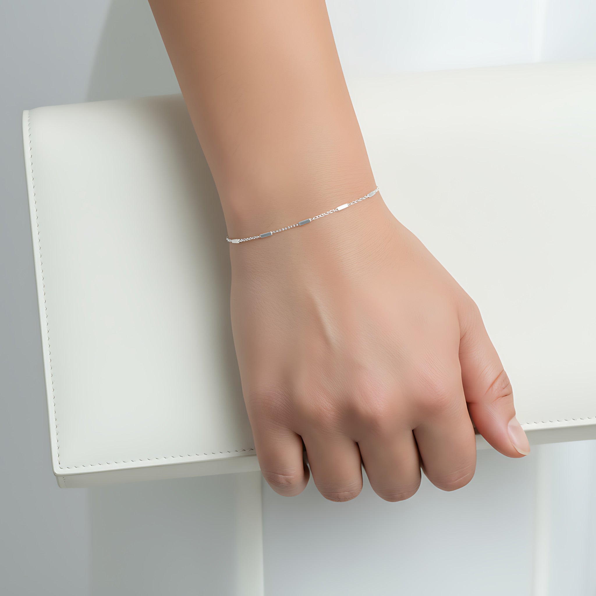 Silver bar bracelet on a person's wrist holding a white clutch with a white background