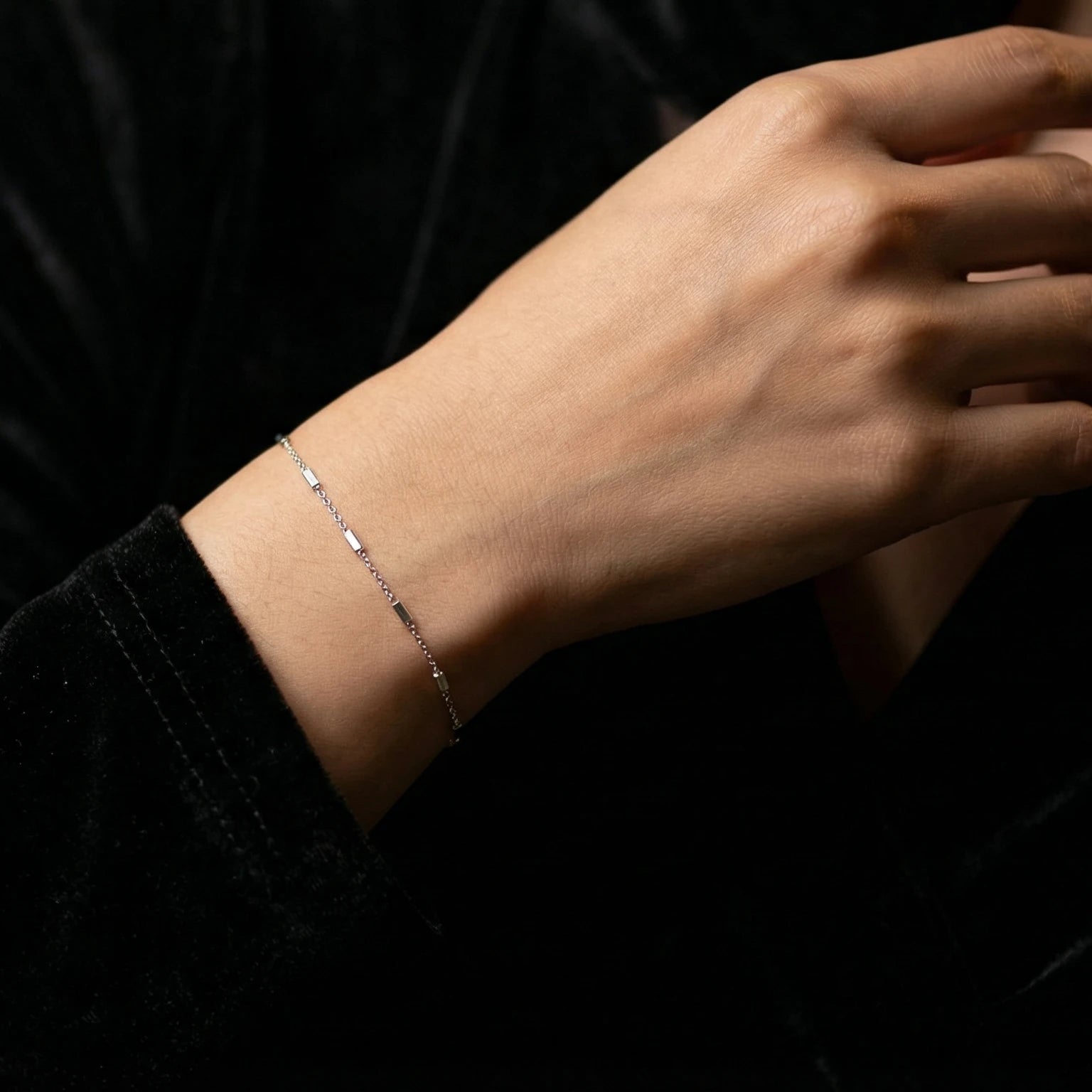 Silver bar bracelet on a person's wrist against a dark background
