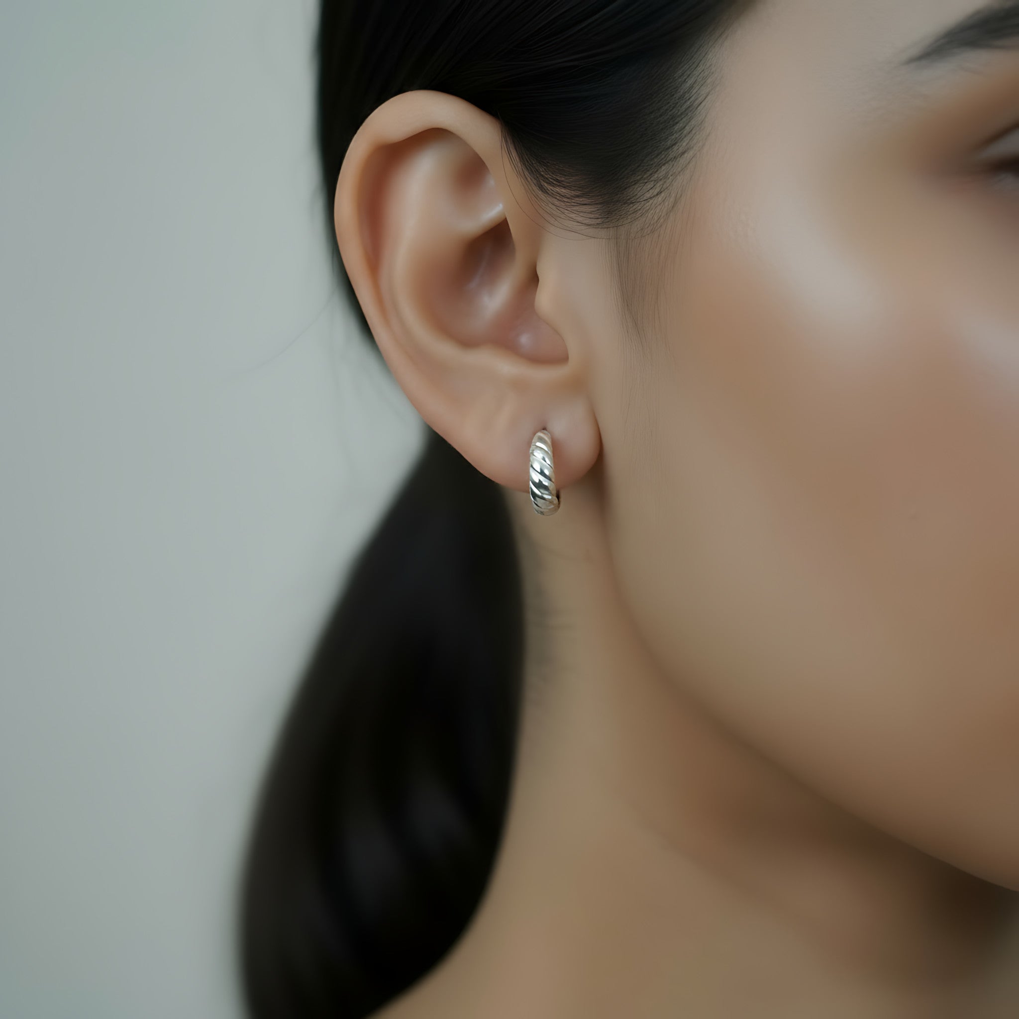 Close-up of an ear wearing a silver  croissant style half hoop stud earring with a blurred background