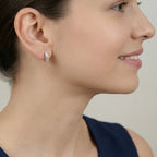 Close-up of an ear wearing a silver  croissant style half hoop stud earring with a neutral background