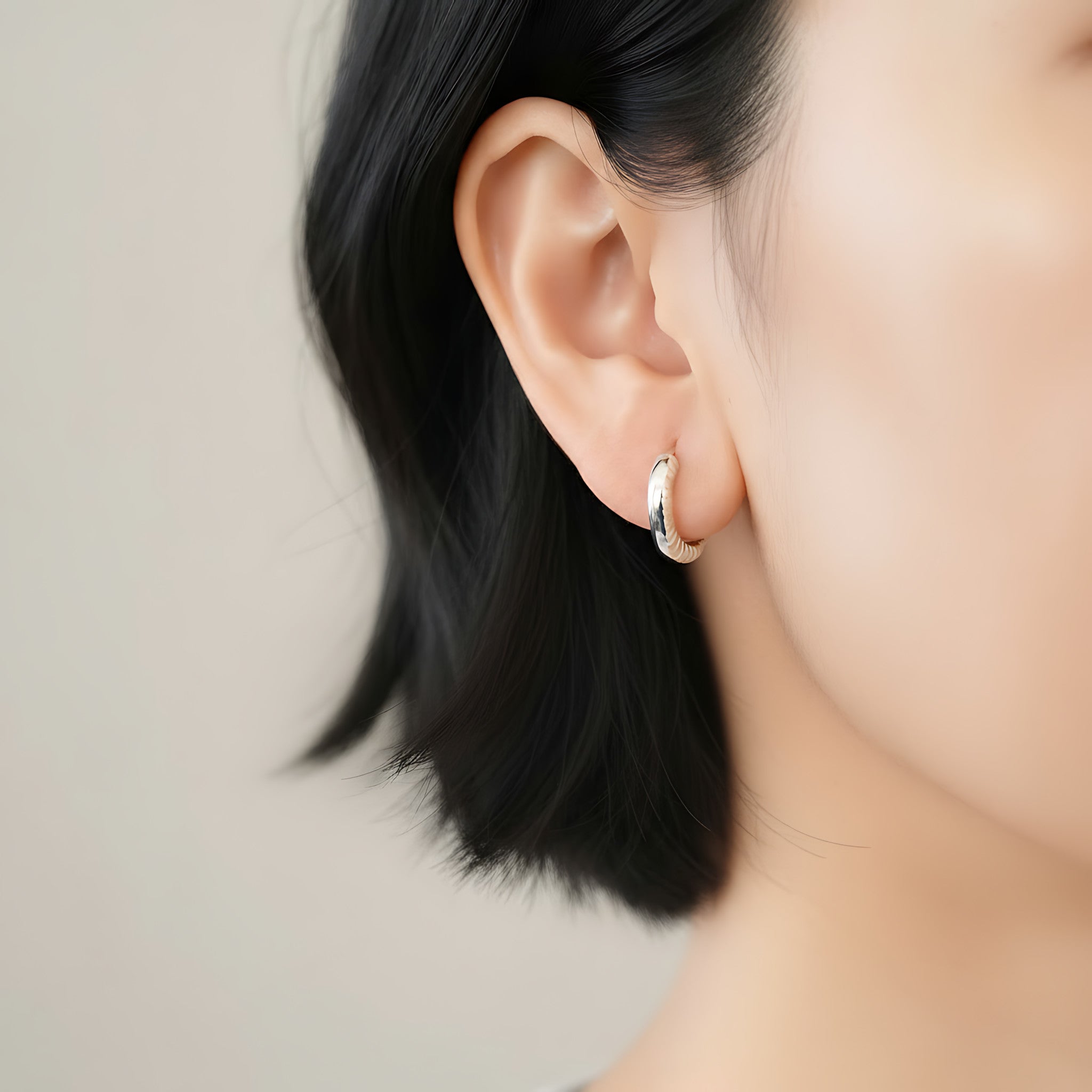 Close-up of an ear wearing a chunky silver hoop earring with side cuts on a neutral background
