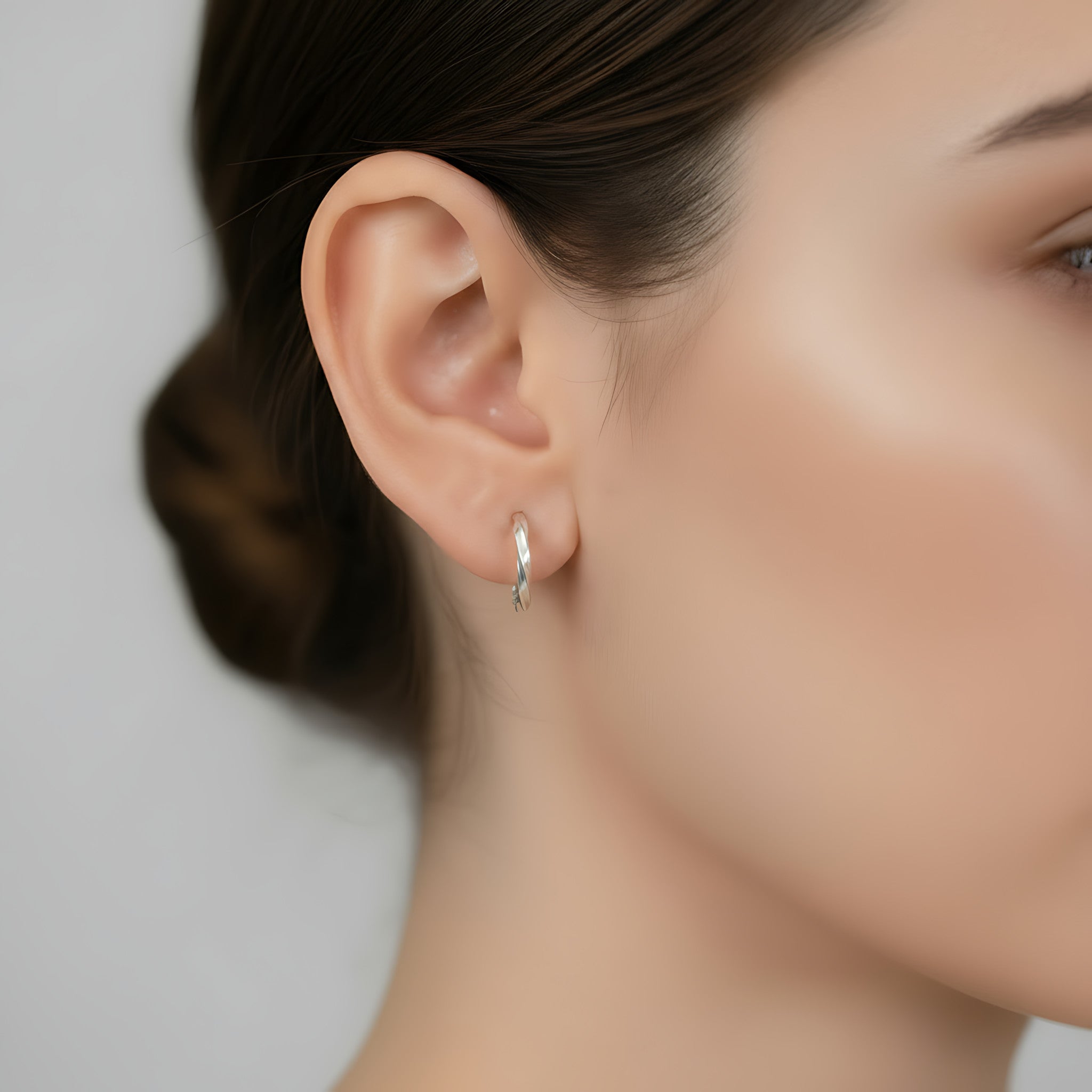 Close-up of a woman wearing a silver twisted half hoop stud earring against a neutral background