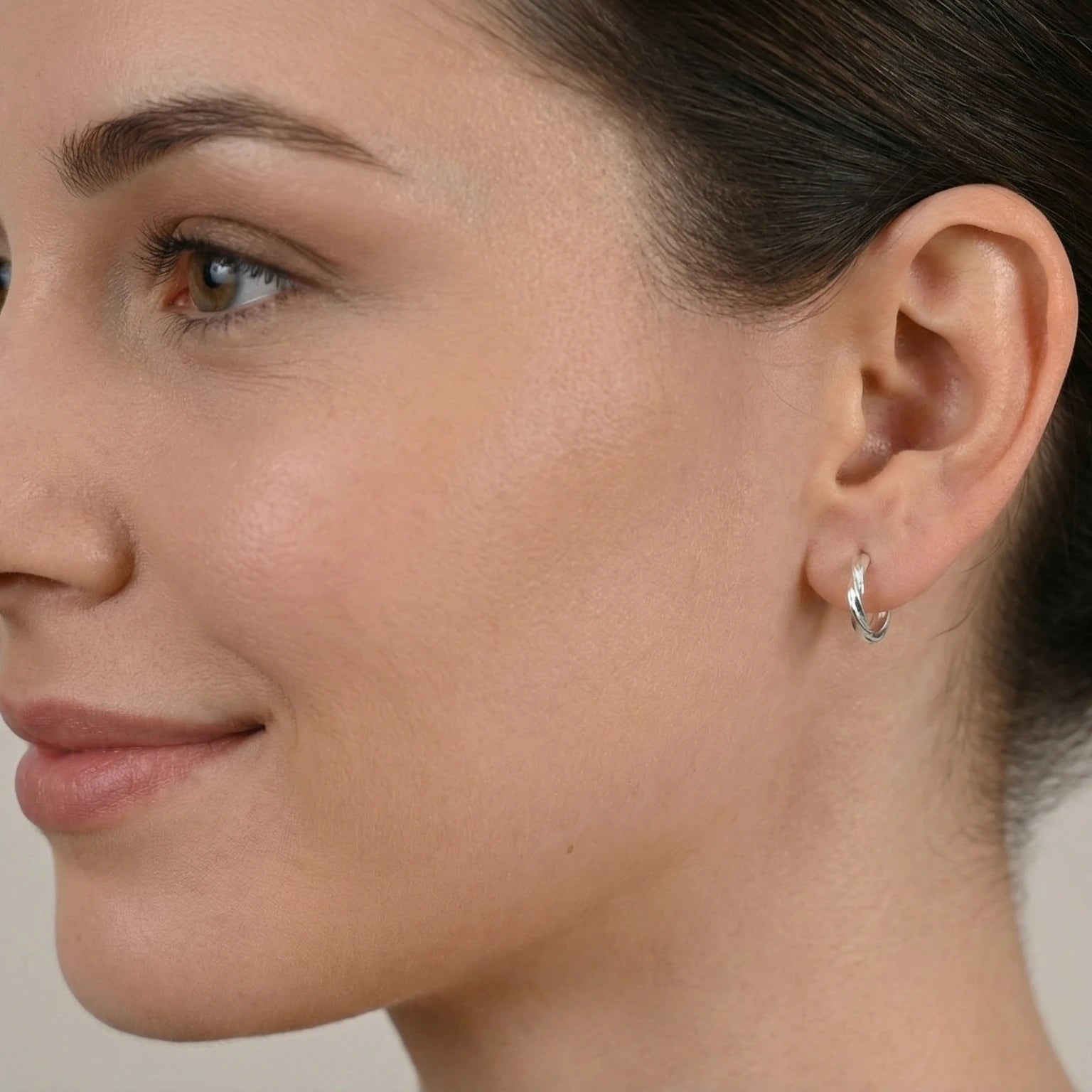 Close-up of a woman wearing a silver twisted half hoop stud earring against a neutral background
