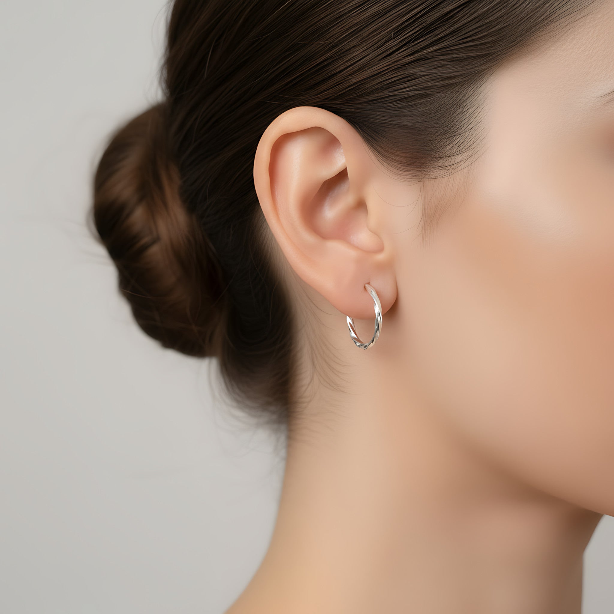 Close-up of a woman wearing a silver twisted half hoop stud earring with a neutral background