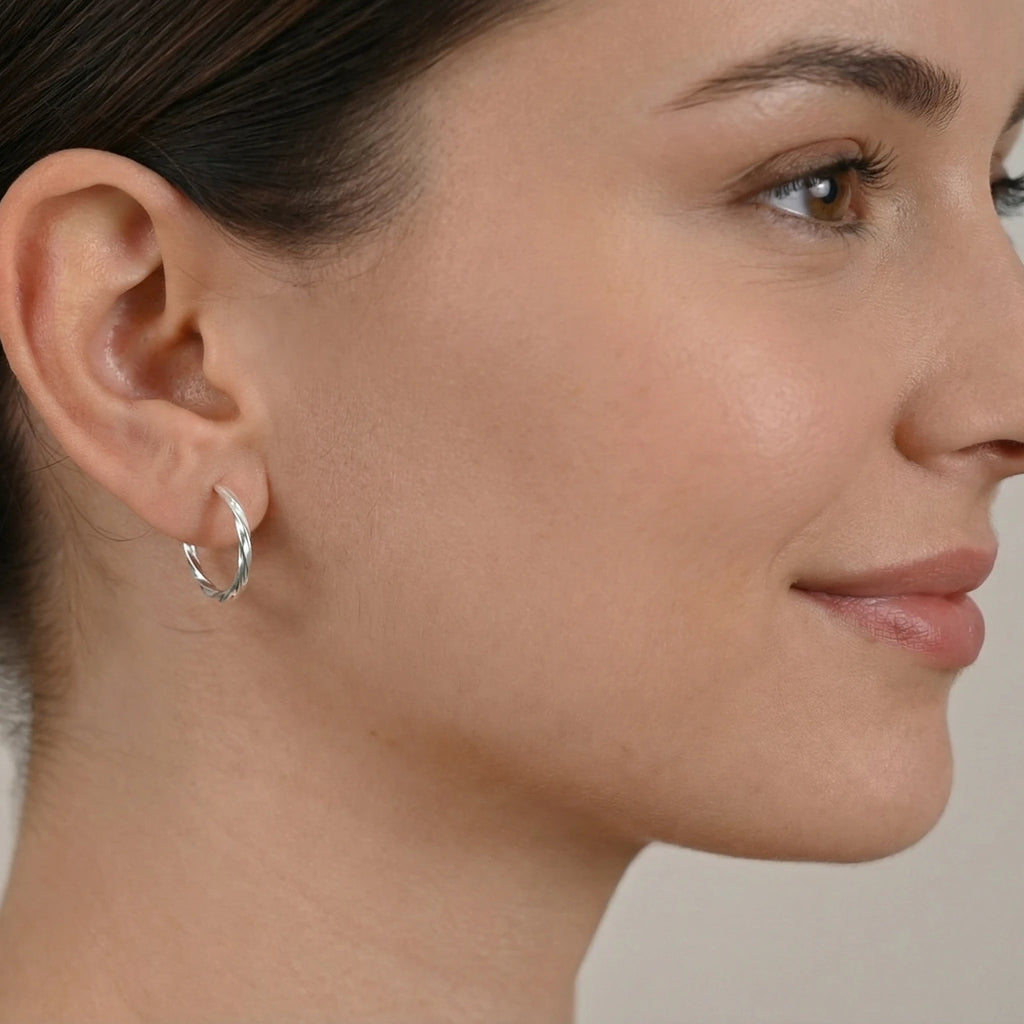 Close-up of a woman wearing a silver twisted half hoop stud earring against a neutral background
