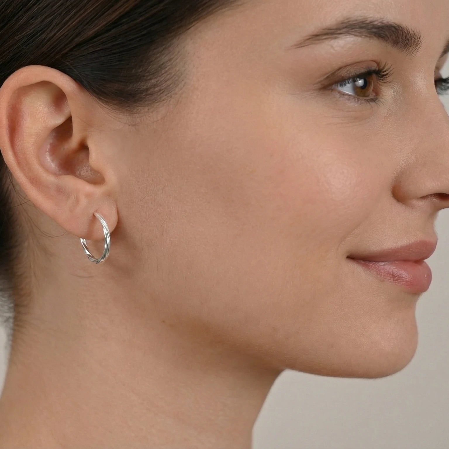 Close-up of a woman wearing a silver twisted half hoop stud earring against a neutral background