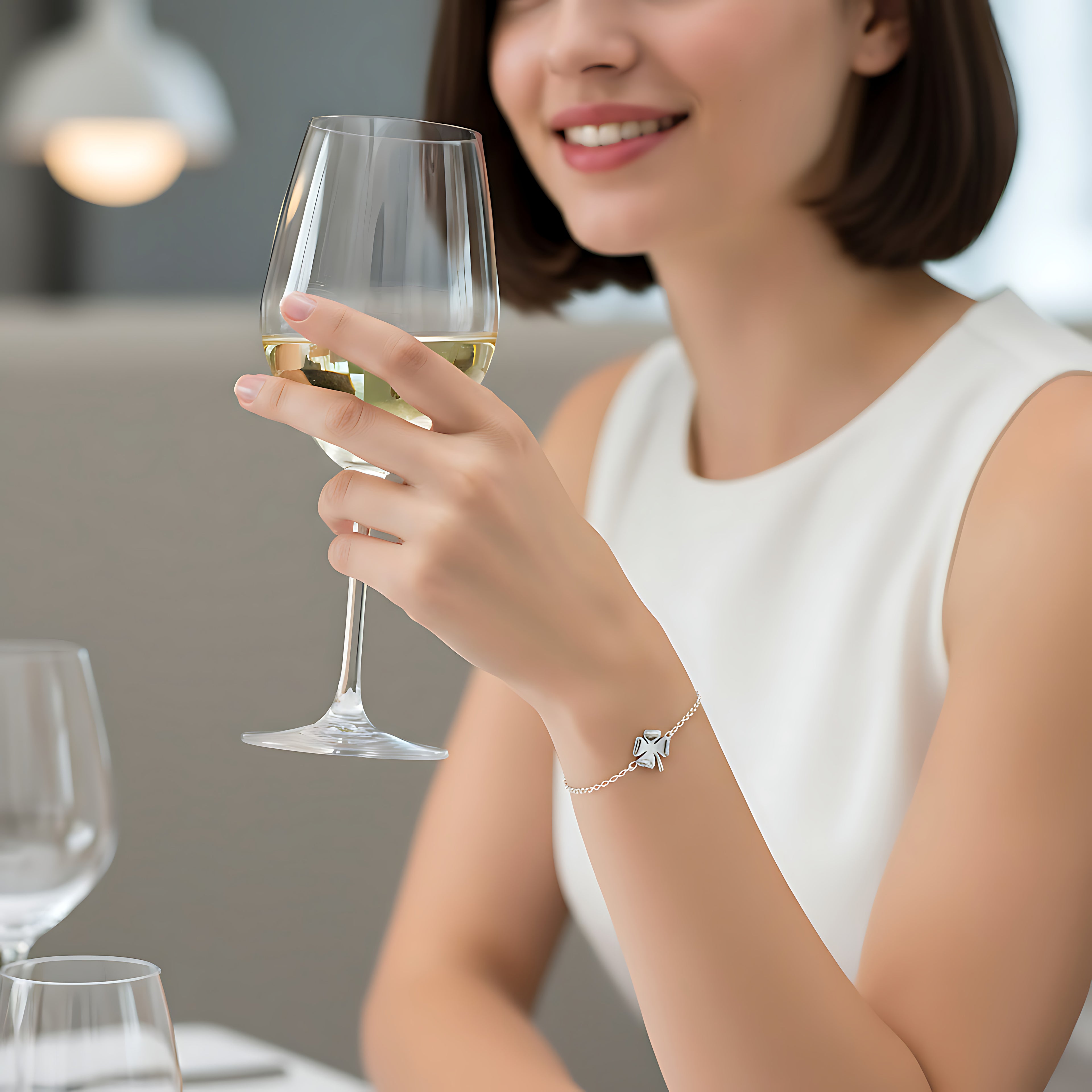 Woman holding a glass of white wine with a blurred background wearing a delicate silver clover bracelet
