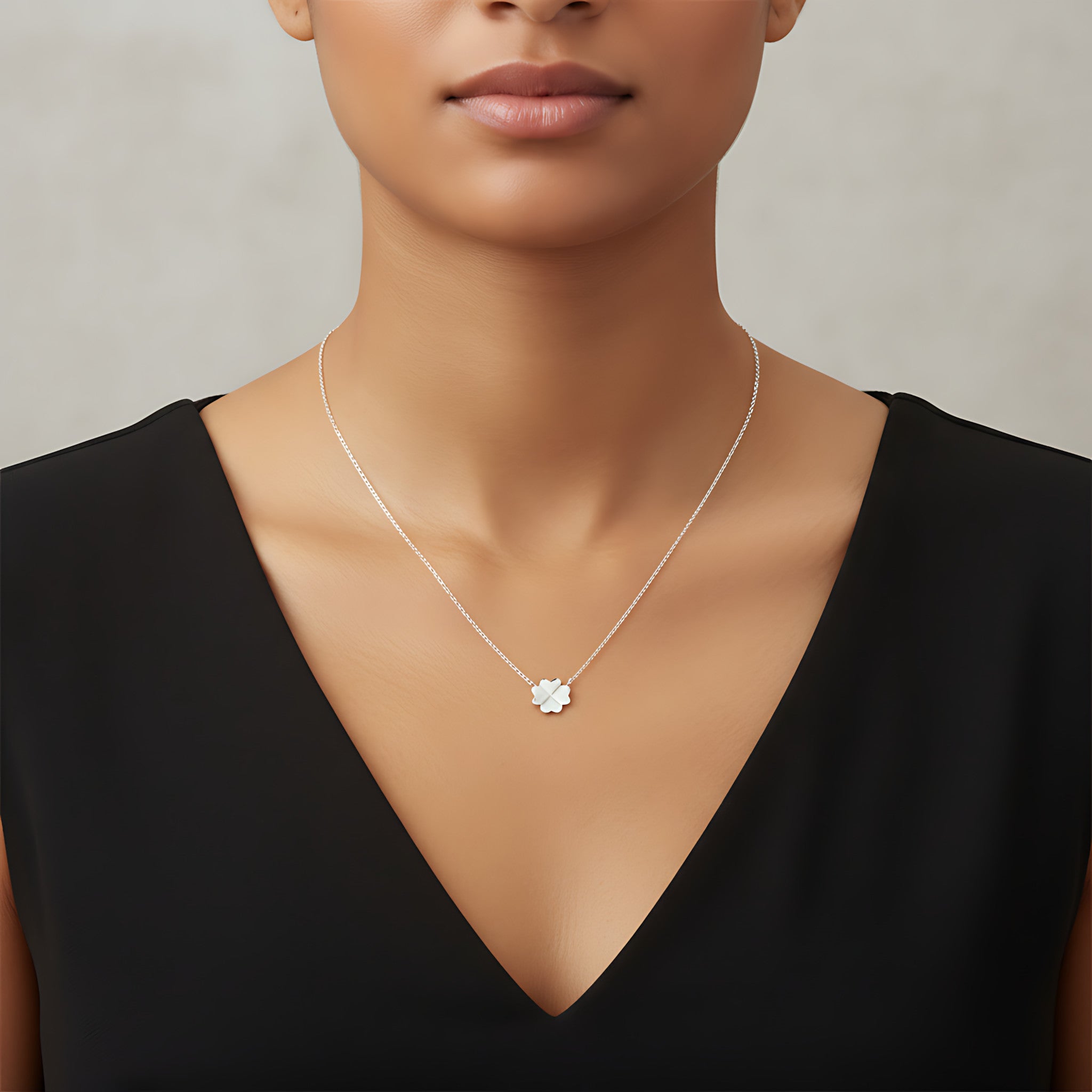 Closeup of a female wearing a silver necklace with a small clover pendant against a neutral background