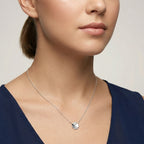 Closeup of a female wearing a silver necklace with a small clover pendant against a neutral background