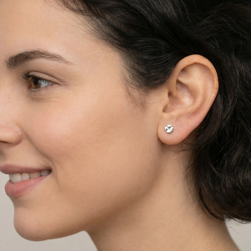 Woman with short dark hair wearing silver clover stud earring standing in a garden with blurred greenery