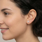 Woman with short dark hair wearing silver clover stud earring standing in a garden with blurred greenery