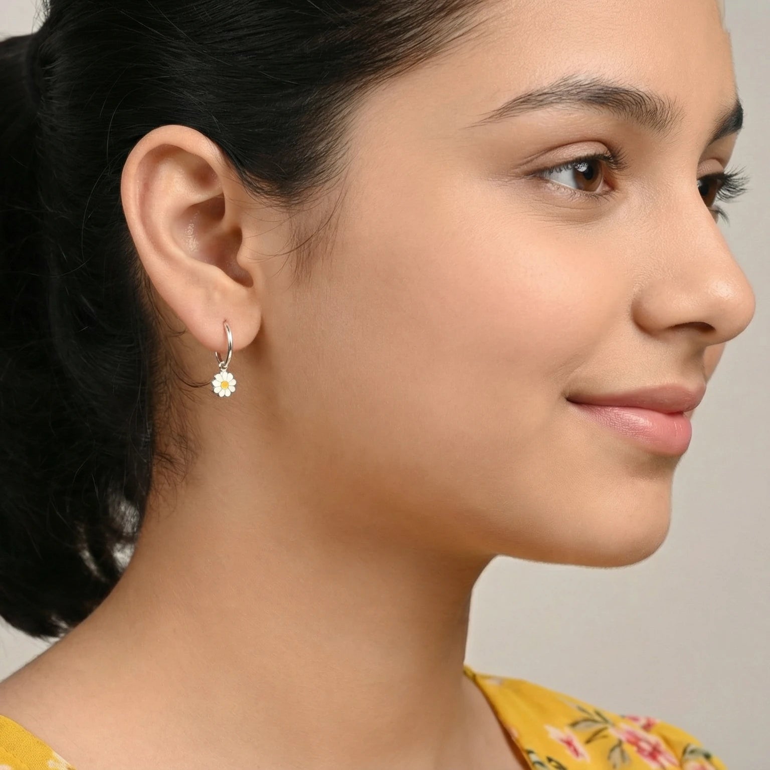 Closeup of a girl wearing a silver flower charm hoop earring on a plain background