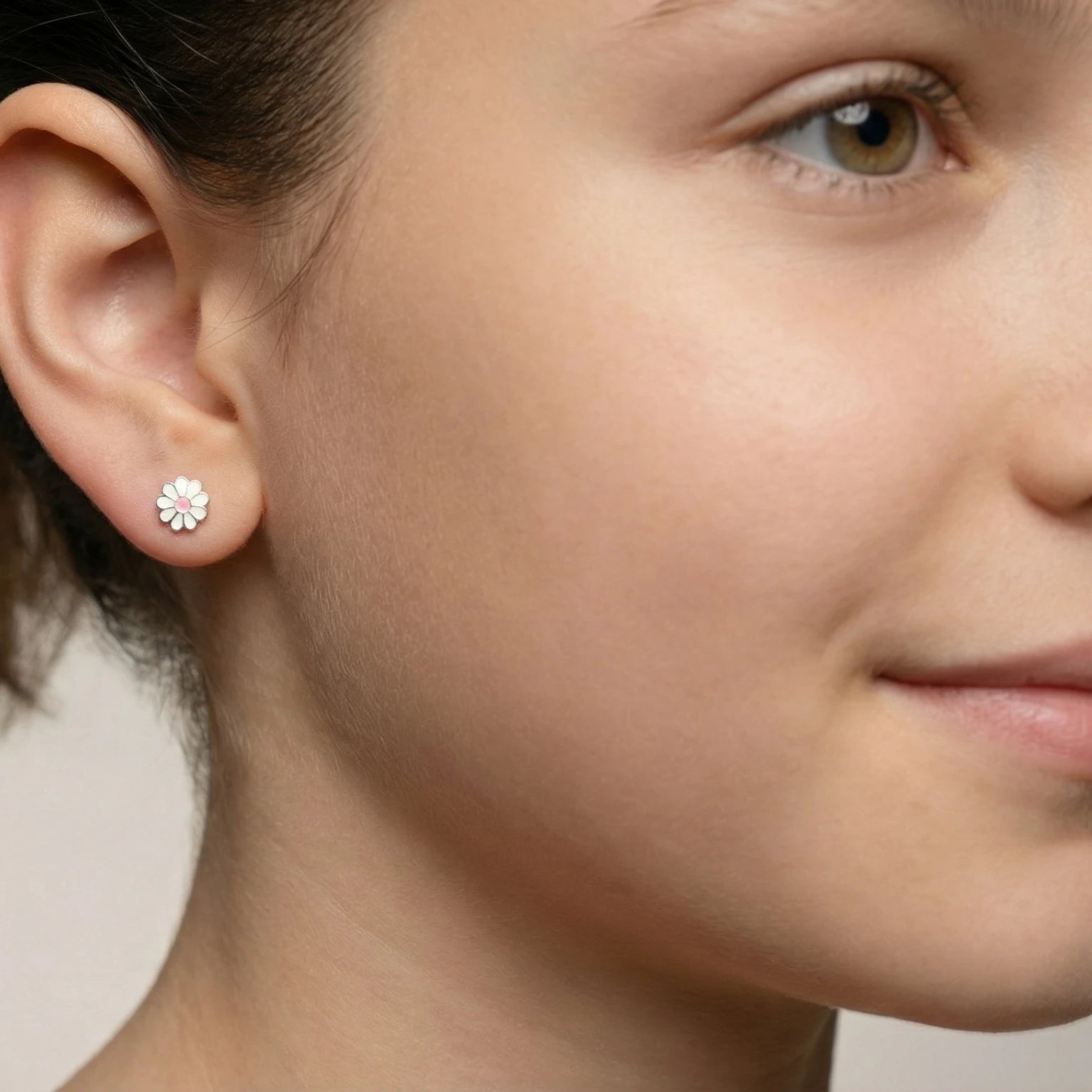 A girl wearing silver flower stud earrings against a blurred neutral background