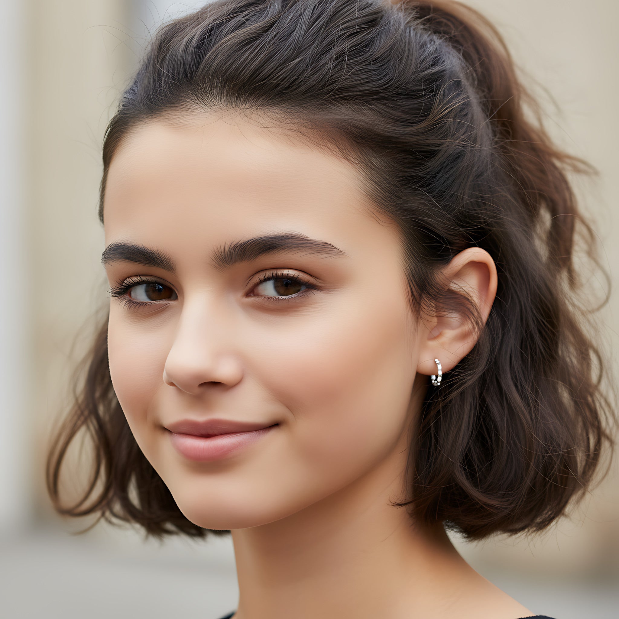 Close-up of a young girl with styled hair and silver diamond cut half hoop stud earrings against a neutral background