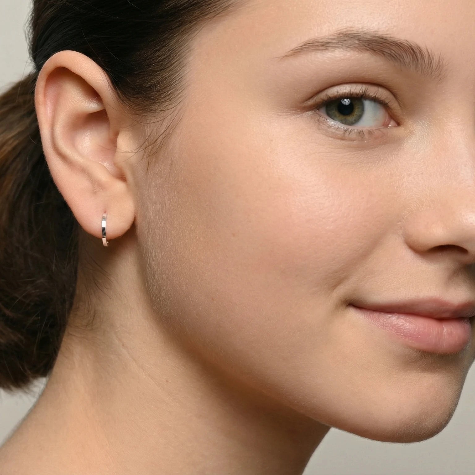 Close-up of a young girl  wearing silver diamond cut half hoop stud earrings against a neutral background