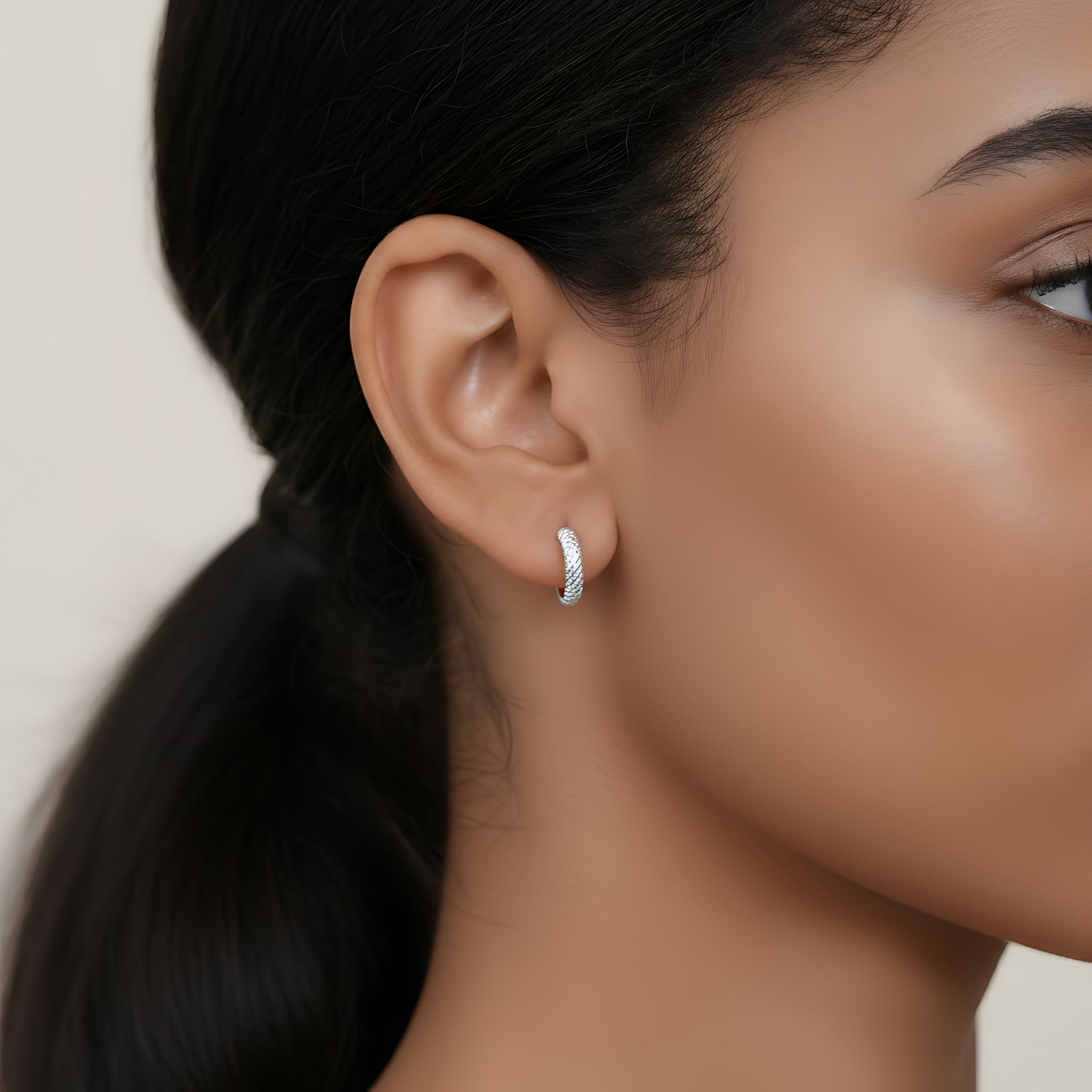 Silver hoop earring with diamond cut texture worn by a person with a neutral background