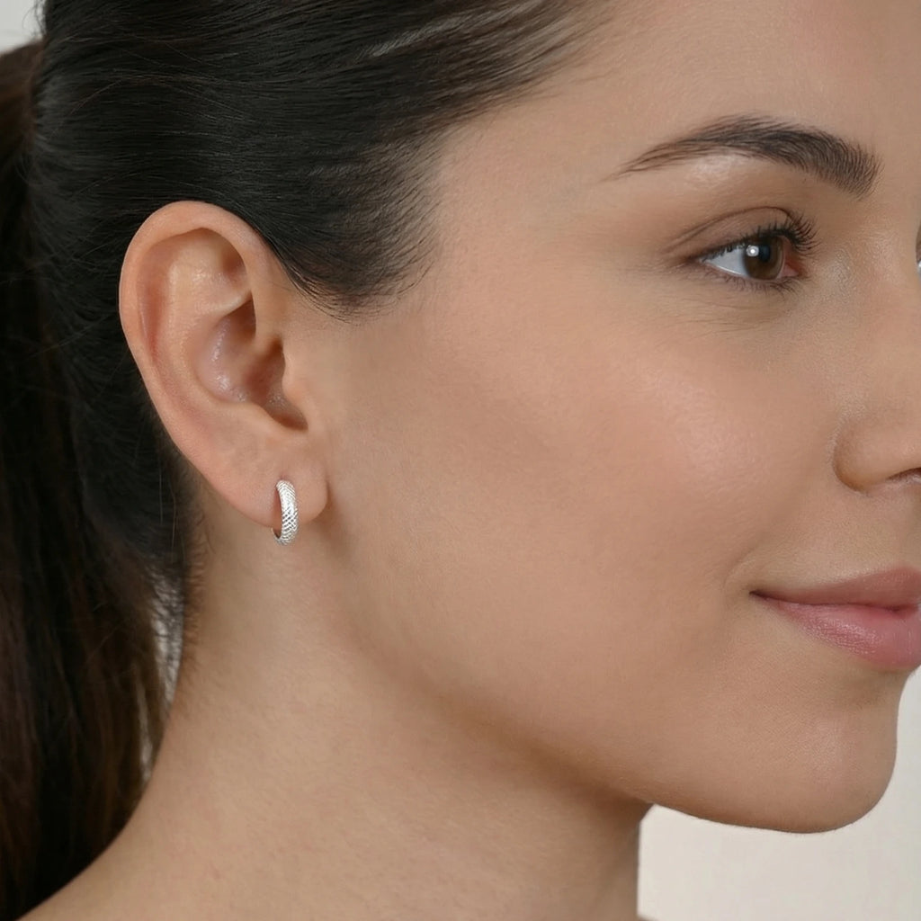 Silver hoop earring with diamond cut texture worn by a female with a neutral background