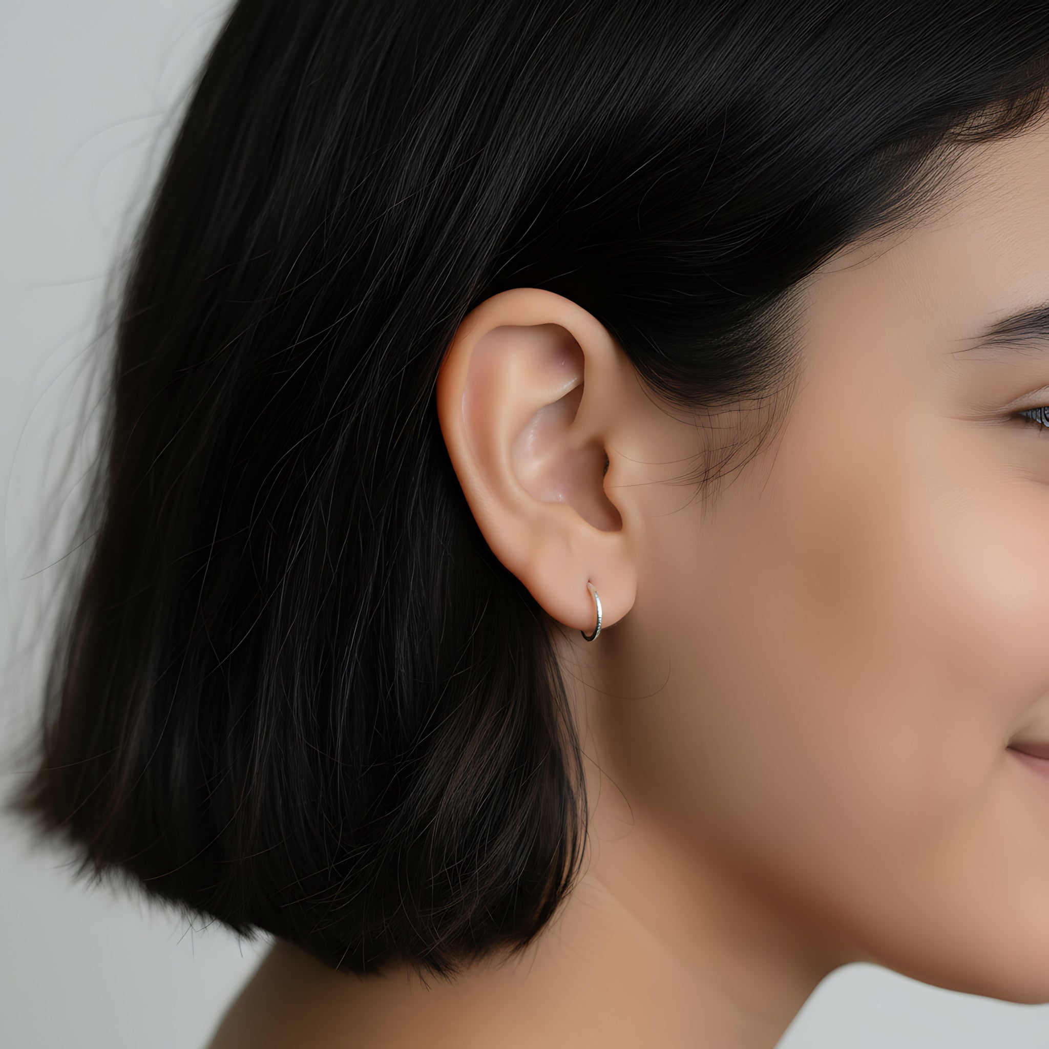Close-up of a young girl wearing a silver diamond dust half hoop stud earrings against a neutral background