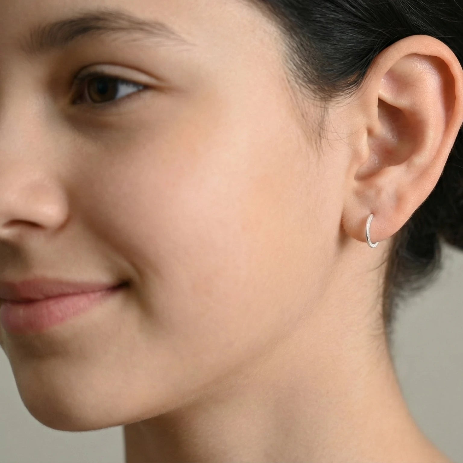 Close-up of a young girl wearing a silver diamond dust half hoop stud earrings against a neutral background