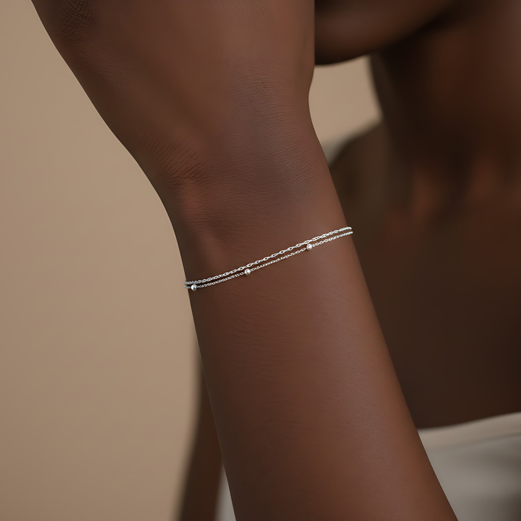 Silver double chain bracelet on a person's wrist against a neutral background