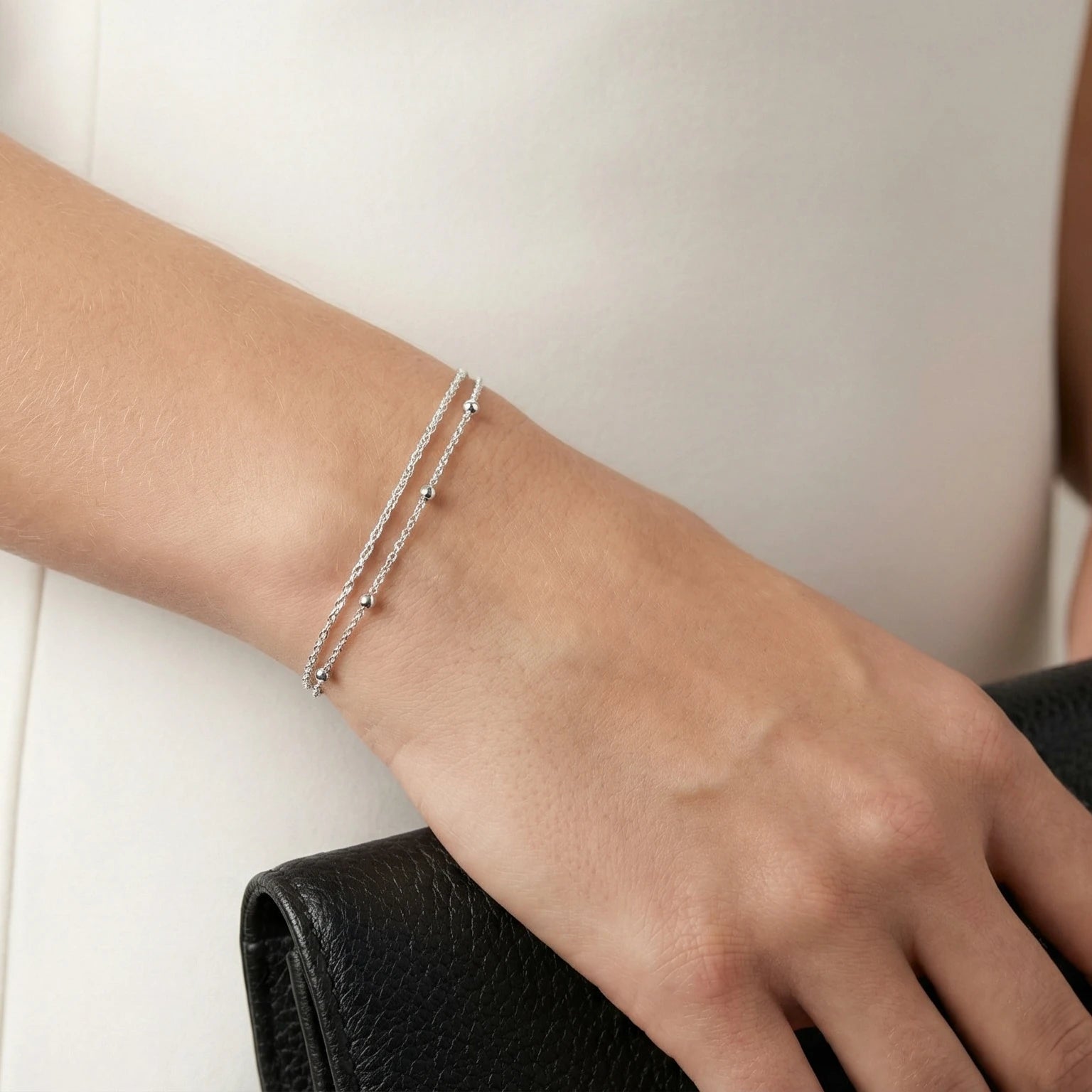 Double Chain Silver bracelet on a wrist while holding a black clutch wearing a white dress
