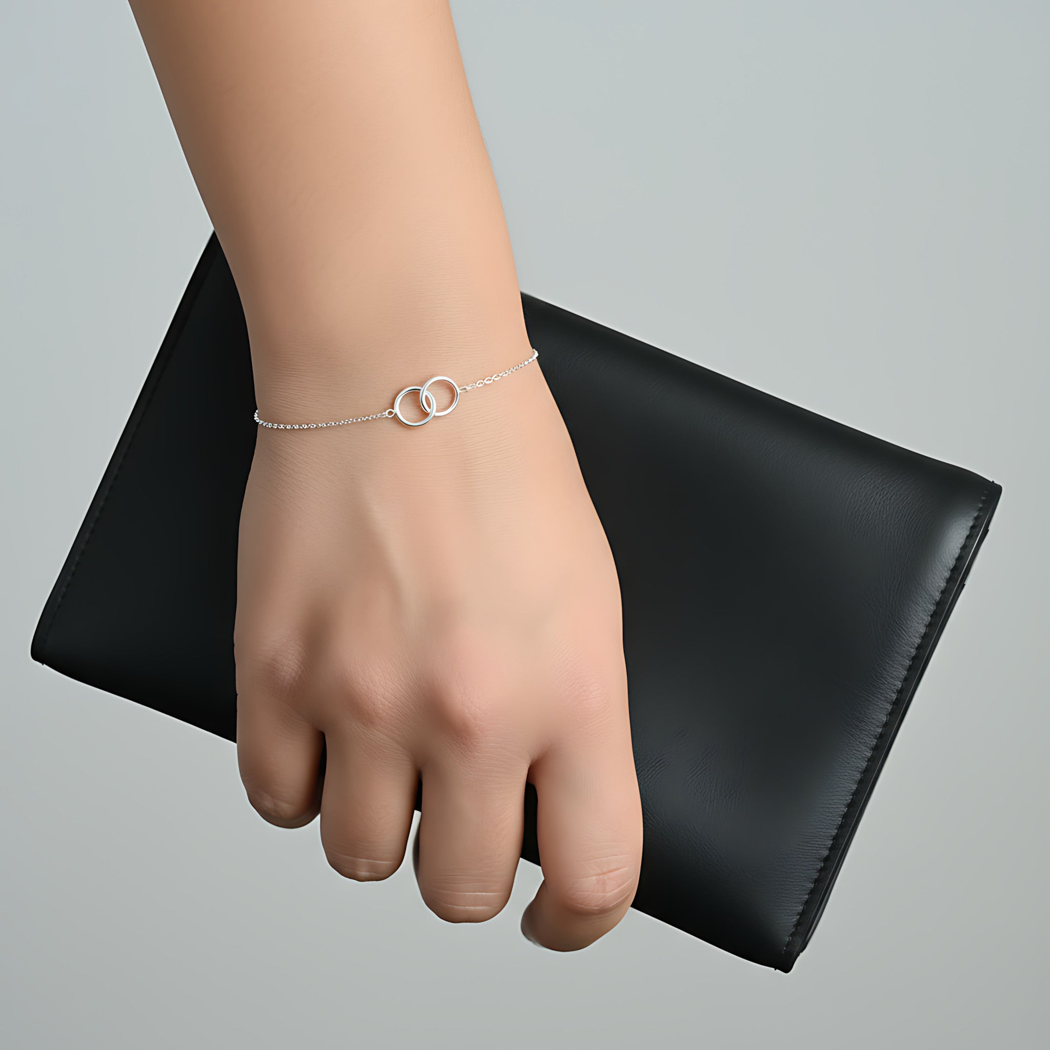 Hand wearing a silver intertwined circles bracelet with a black clutch on a gray background
