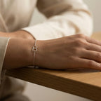Close-up of a hand wearing a silver bracelet with 2 circle charms on a wooden surface