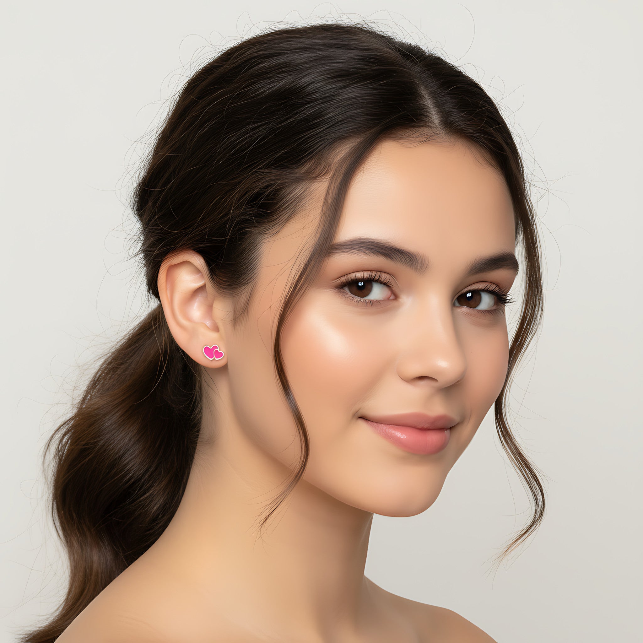 A girl wearing pink double heart-shaped earrings on a plain background