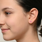 A girl wearing pink double heart-shaped earrings on a plain background