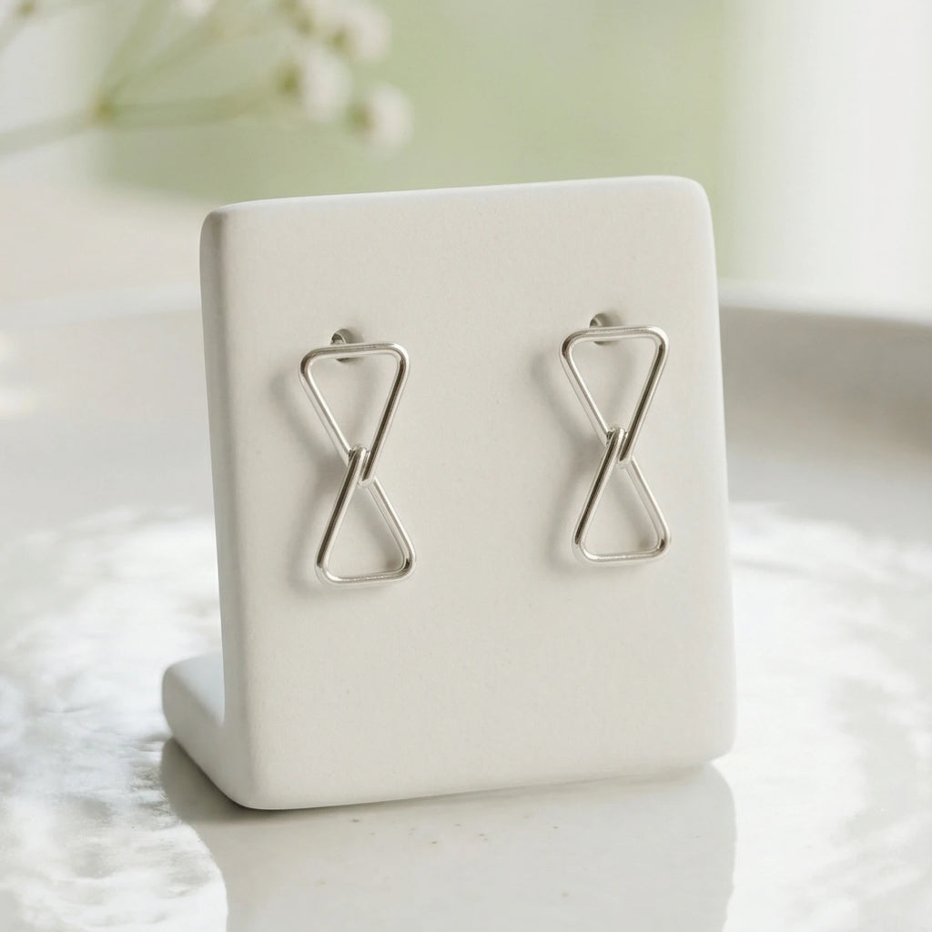 Silver hourglass-shaped earrings on a white jewelry stand with a light background