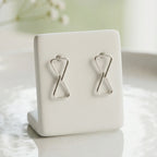 Silver hourglass-shaped earrings on a white jewelry stand with a light background