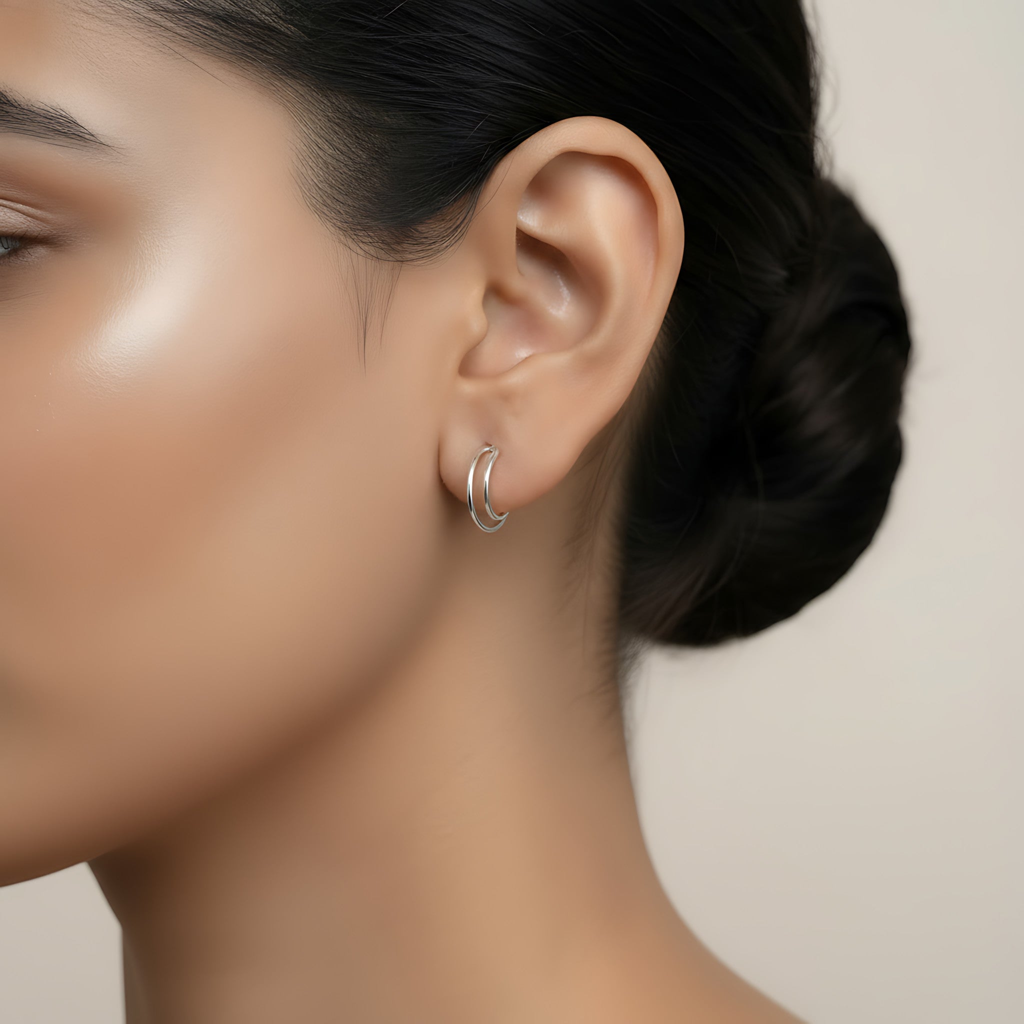 Close-up of an ear wearing a silver dual band half hoop stud earring with a neutral background